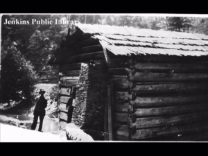 A photo of a log cabin.  The photograph was found in the Jenkins Public Library by Ernie Bentley.